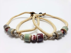 Cream cord wrap bracelet with multicolored ceramic beads and silver spacers on a white background.