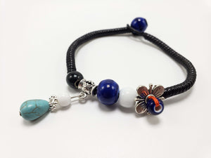 Black cord bracelet with blue and white beads, turquoise teardrop charm, and silver flower accent.