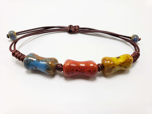 Brown cord bracelet with three multicolored ceramic beads (blue, red, yellow) on a white background.
