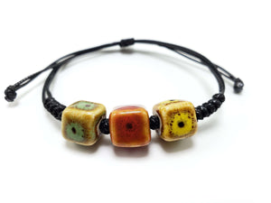 Black cord bracelet with three square ceramic beads in green, rust, and yellow.