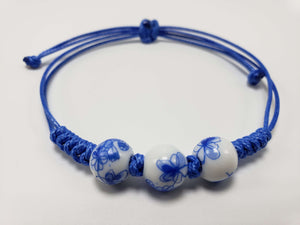 Blue adjustable cord bracelet with three white ceramic beads decorated with blue floral patterns.