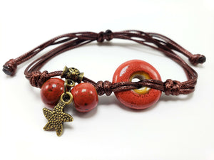 Handmade brown cord bracelet with orange ceramic beads and a bronze star charm on a white background.