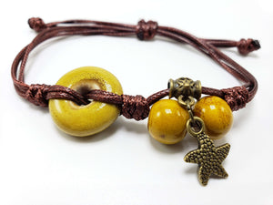 Handmade brown cord bracelet with yellow ceramic beads and a bronze star charm on a white background.
